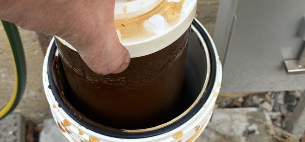 A used brown sediment cartridge being lifted out of its housing during a filter change