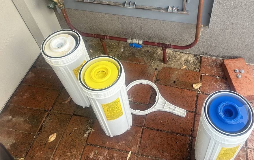 Complete Home Filtration cartridges in their housings: white sediment, yellow resin and blue carbon, yellow marked